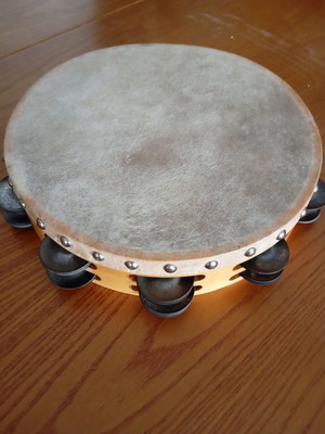 Tambourine used with natural skin, wooden frame, and metal jingles
