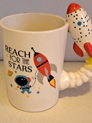 Ceramic space-themed mug with 3D rocket handle and Reach for the Stars phrase