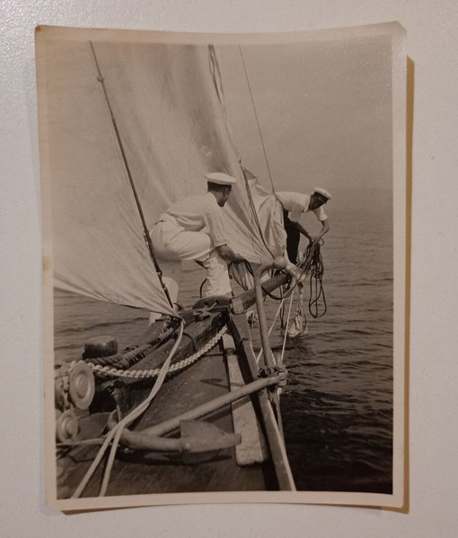 Σχετικά μικρή, παλιά, ασπρόμαυρη φωτογραφία με βάρκα στη θάλασσα και δύο άντρες εν ώρα εργασίας.