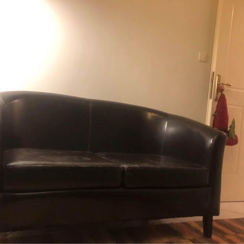 Two-seater black faux leather sofa used with some cushion wear