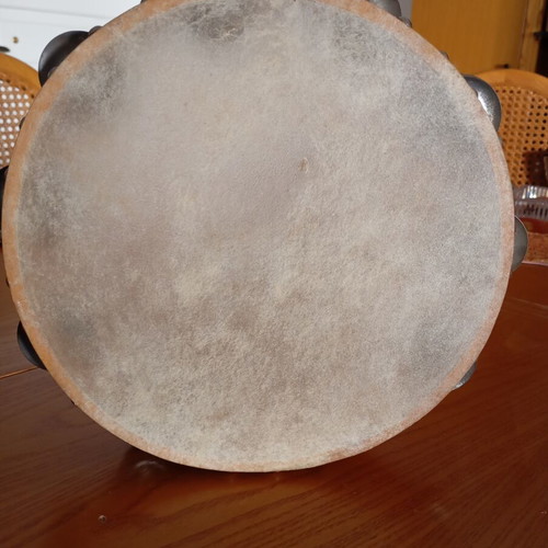 Tambourine used with natural skin, wooden frame, and metal jingles