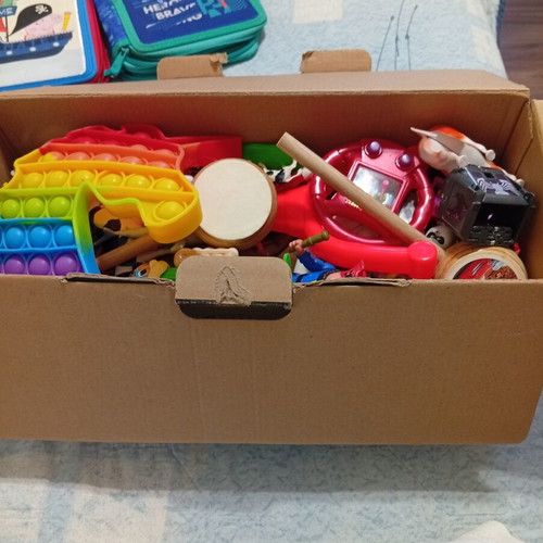 Box of various used children's toys including pop-it and wooden drum