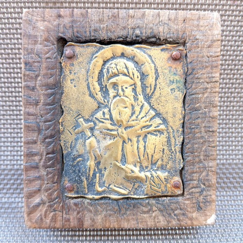 Old brass icon of Saint Anthony in carved wooden frame, used