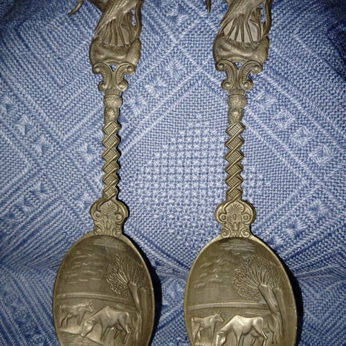 Two large decorative pewter spoons used with intricate animal designs
