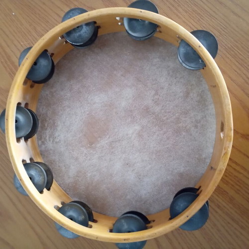 Tambourine used with natural skin, wooden frame, and metal jingles