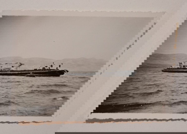 Μικρή, παλιά, ασπρόμαυρη φωτογραφία, με βαρκούλα και καράβι. Άγνωστο το μέρος και η χρονολογία.