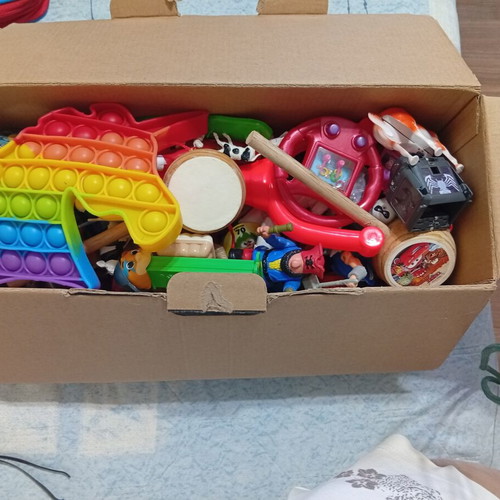 Box of various used children's toys including pop-it and wooden drum
