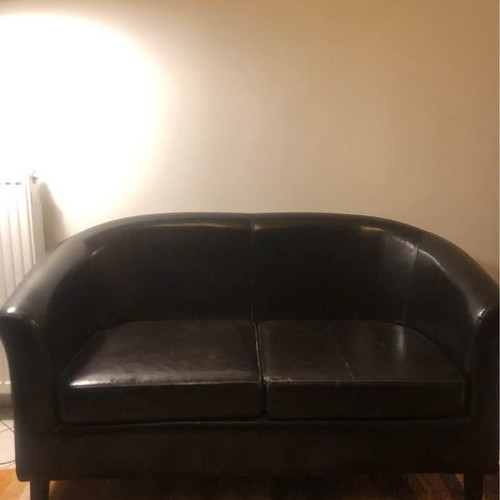 Two-seater black faux leather sofa used with some cushion wear