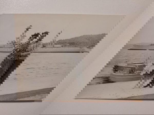 Μικρή, παλιά, φωτογραφία, με ζευγάρι να απολαμβάνει τη βόλτα στη θάλασσα, με θέα βάρκες και καράβια.
