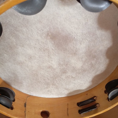 Tambourine used with natural skin, wooden frame, and metal jingles