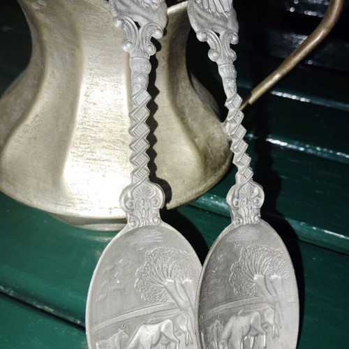 Two large decorative pewter spoons used with intricate animal designs