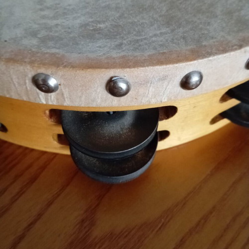 Tambourine used with natural skin, wooden frame, and metal jingles